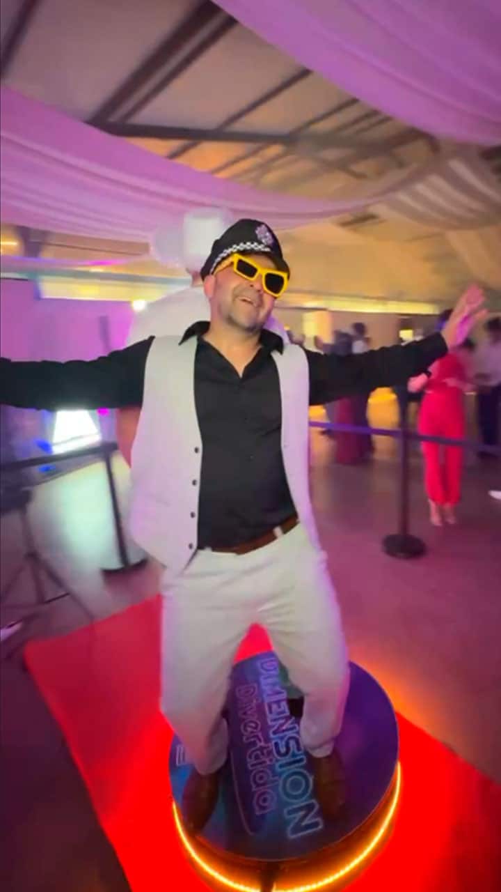 Hombre disfrutando al máximo con gorro de capitán y gafas amarillas sobre la plataforma Videomatón 360 de Dimensión Divertida. Alquiler de plataforma 360 para eventos y fiestas en Girona.