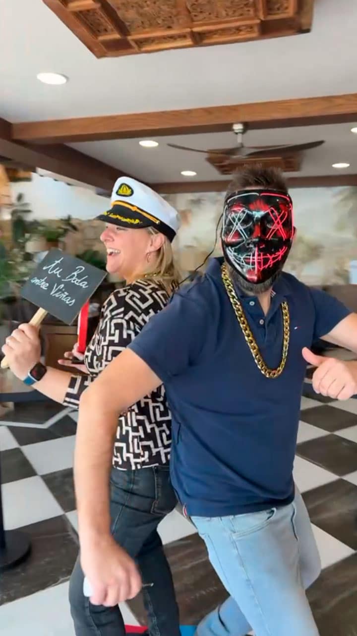 Pareja disfrazada divirtiéndose con máscara luminosa, gorro de capitán y collar de oro en la plataforma 360. Alquiler de Dimensión Divertida para fiestas temáticas en Barcelona.